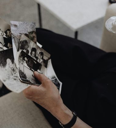 A person reflecting on memories while holding photographs and a wine glass.